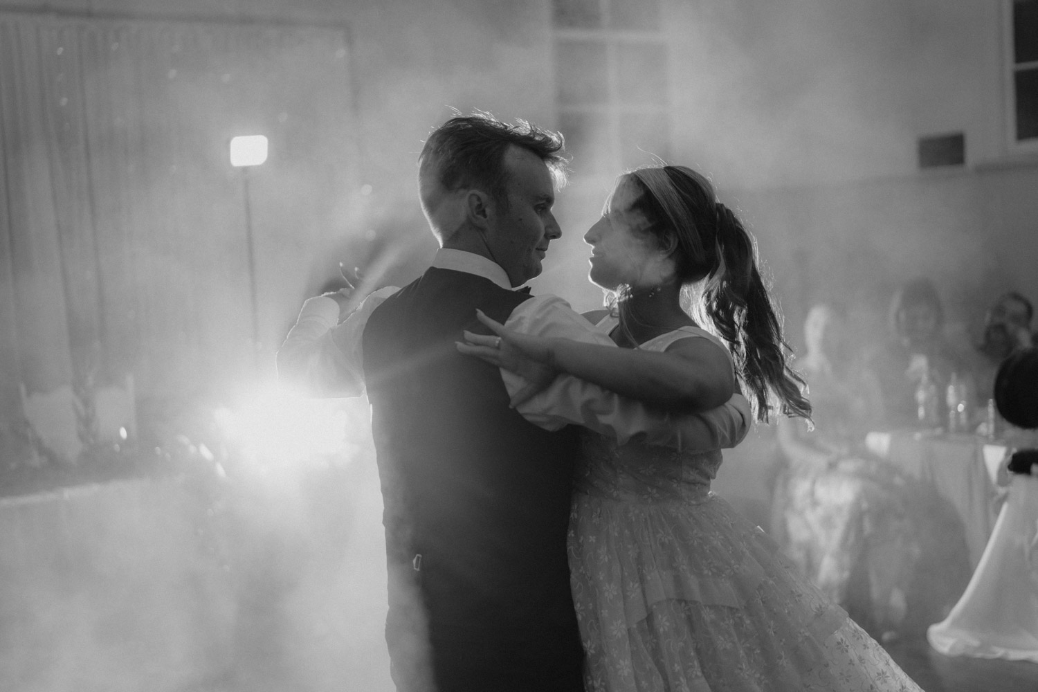 In a misty, ethereal setting, a bride and groom share a dance, their silhouettes illuminated by backlight, showcasing the romantic and LaterStory affordable wedding photography that captures the magic of their day