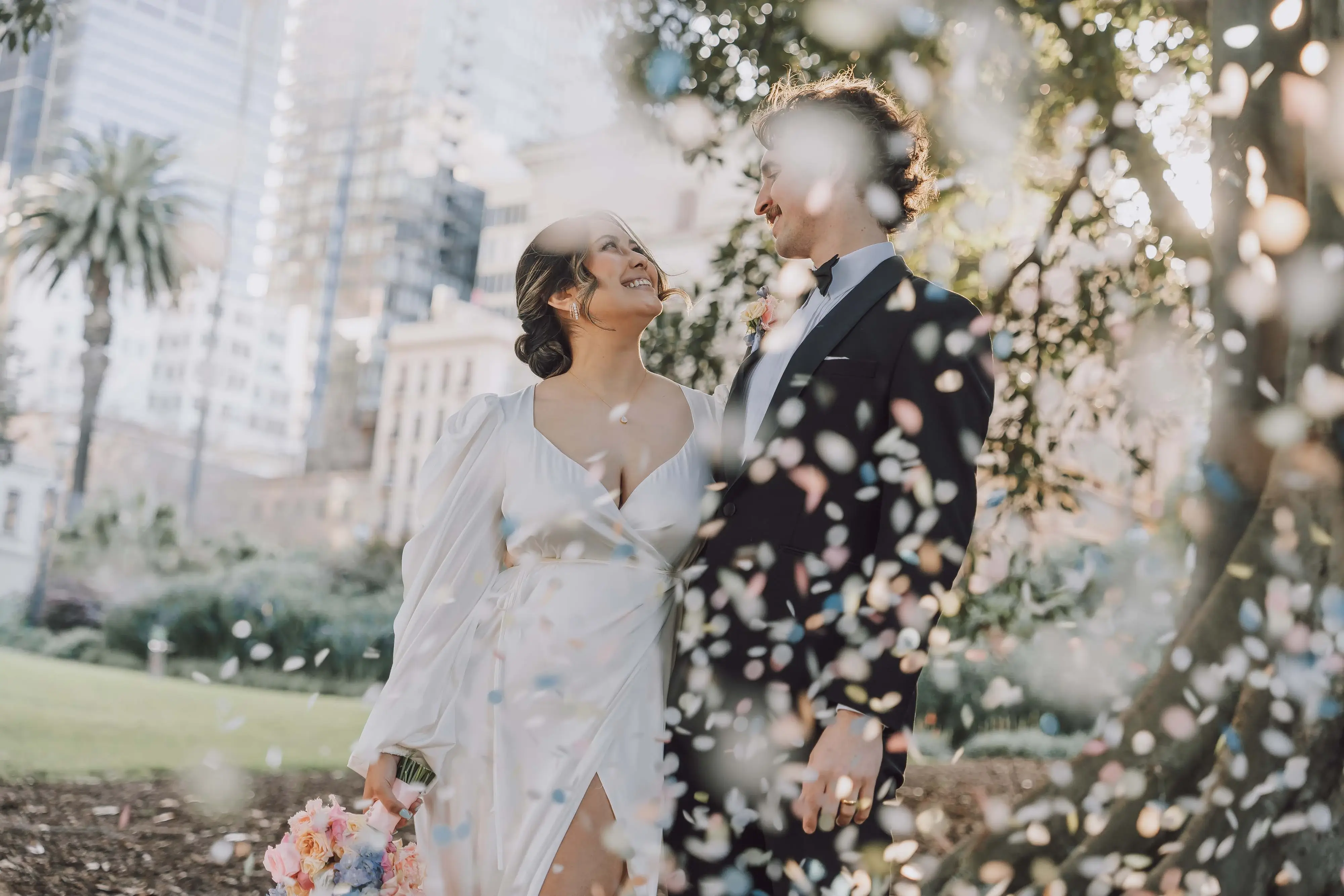 Bride and groom sharing a tender moment surrounded by falling petals in a Melbourne park, epitomizing the art of wedding photography Melbourne.